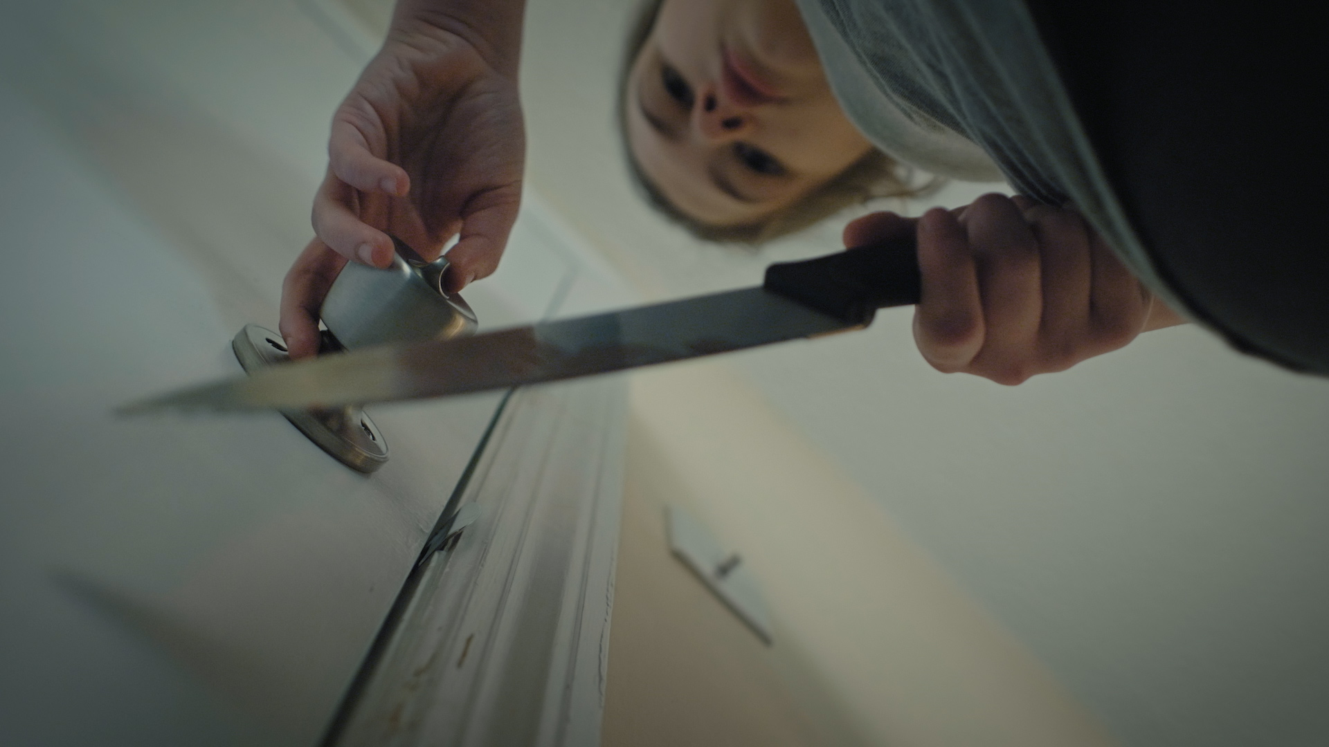 Clara approaches a door with a knife in hand