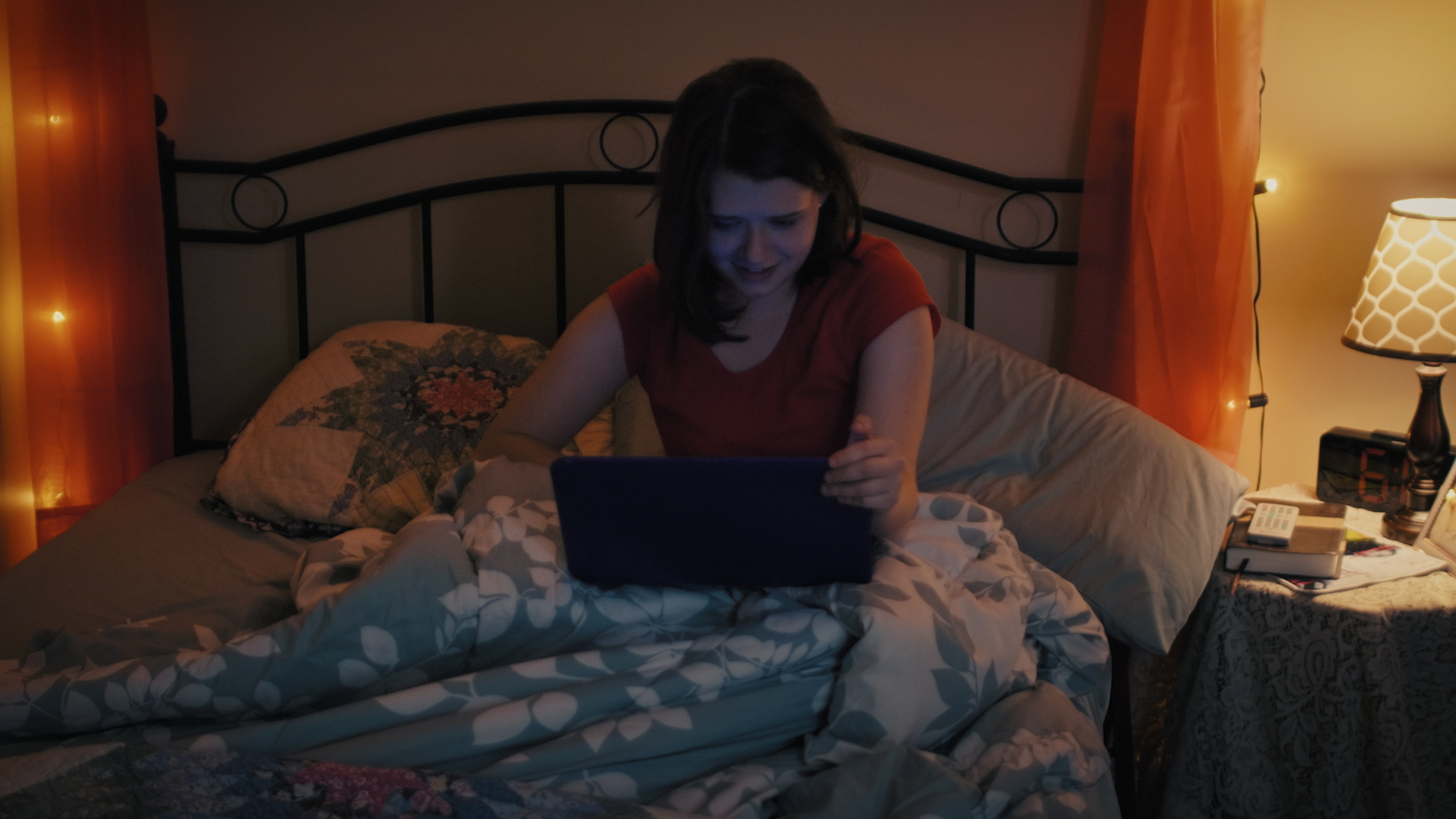 Clara opens her laptop up while laying in bed